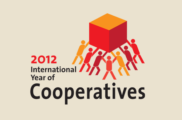 The logo of international year of cooperatives. Several figures lift up a red cube.